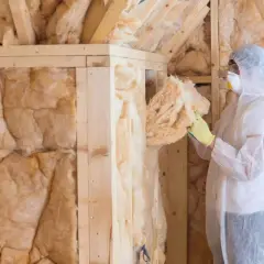 Ocieplenie domu drewnianego wełną mineralną krok po kroku. Pracownik w kombinezonie montuje wełnę w drewnianej konstrukcji.