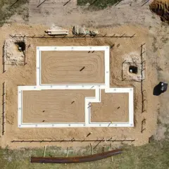 Widok z lotu ptaka na plac budowy z fundamentami. Różne rodzaje fundamentów są widoczne, w tym ławy fundamentowe i wykopy pod słupy.