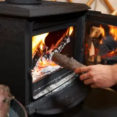 Dłoń wkłada drewno do płonącego pieca. W piecu można palić drewnem, by ogrzać dom.