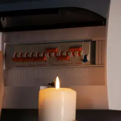 Kobieta sprawdza bezpieczniki przy świecy. Brak prądu w gniazdkach, ale bezpieczniki ok.