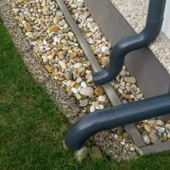 Szare rury odprowadzają wodę z rynien na kamieniste podłoże. Zapewniają prawidłowe odprowadzenie wody z rynien, zgodnie z przepisami.
