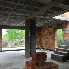 Budowa domu w stanie surowym. Widać betonowy strop typu ackerman, ściany z pustaków ceramicznych, schody i materiały budowlane.
