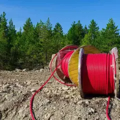 Uzbrojenie działki krok po kroku: duża szpula z czerwonym kablem leży na kamienistym terenie, w tle las i błękitne niebo.