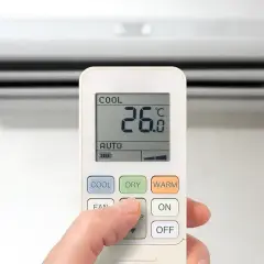 Dłoń steruje pilotem klimatyzacji, wybierając funkcje chłodzenia (COOL), osuszania (DRY) lub grzania (WARM), by dostosować temperaturę.