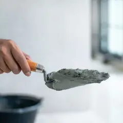 Dłoń trzyma kielnię z masą betonową, przygotowując się do pracy. Dowiedz się, jak zrobić suchy beton.