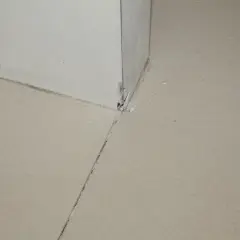 Widok na narożnik ściany i podłogi, gdzie widać, jak zrobić dylatacje w wylewce. Widoczne są szczeliny i fragmenty materiału.