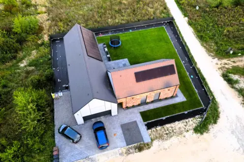 Nowoczesny dom pod klucz, gotowy do zamieszkania. Dwa samochody na podjeździe, panele słoneczne na dachu, zadbany ogród z trampoliną.