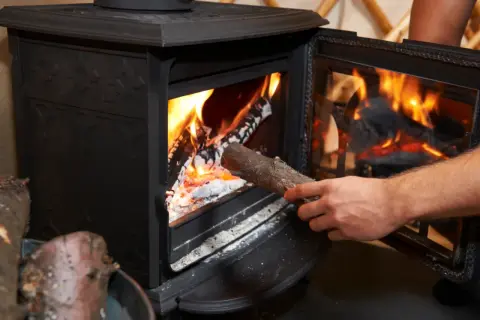 Dłoń wkłada drewno do płonącego pieca. W piecu można palić drewnem, by ogrzać dom.