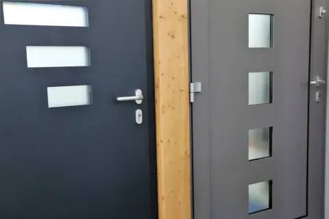 Dwie nowoczesne drzwi wejściowe, ciemnoszare i szare, z przeszkleniami. Dowiedz się, jak uszczelnić drzwi wejściowe, by zapewnić ciepło.