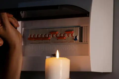 Kobieta sprawdza bezpieczniki przy świecy. Brak prądu w gniazdkach, ale bezpieczniki ok.