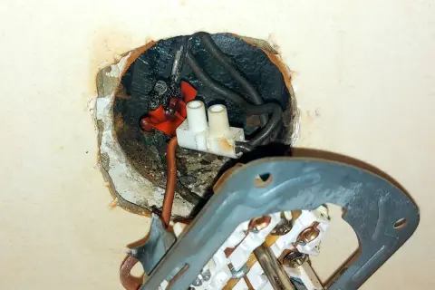 Widoczne iskrzenie w gniazdku, spalone przewody i luźne połączenia. Niebezpieczna sytuacja elektryczna.