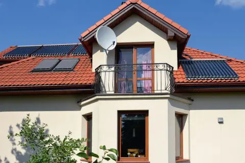 Elegancki wykusz w domu z balkonem i oknami, na dachu panele słoneczne i antenę satelitarną.