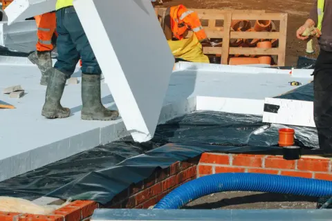 Budowlańcy układają płyty styropianu na stropie betonowym. Dużo styropianu na stropie betonowym to dobra izolacja.