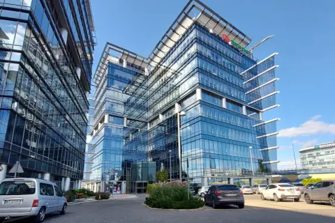 Nowoczesne biurowce ze szklanymi fasadami, odbijające niebo. Na jednym z budynków widoczne logo firmy. Całkowita powierzchnia tych imponujących obiektów robi wrażenie.