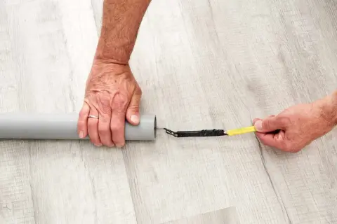 Ręce przygotowują kabel do przeciągnięcia przez peszel. Końcówka kabla owinięta taśmą jest wkładana do szarej rury.