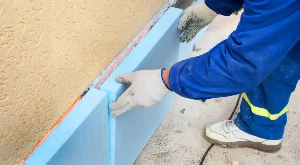Pracownik montuje płyty styroduru o odpowiedniej grubości do ocieplenia fundamentów.