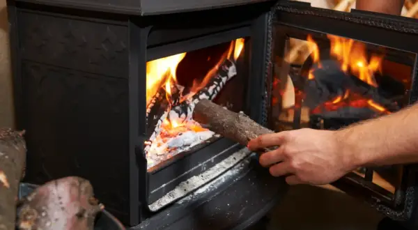 Dłoń wkłada drewno do płonącego pieca. W piecu można palić drewnem, by ogrzać dom.