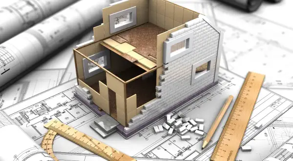 Model domu w przekroju na planach architektonicznych, narzędzia budowlane i małe cegiełki. Wizualizacja projektu budowlanego, który może być początkiem samowoli budowlanej.