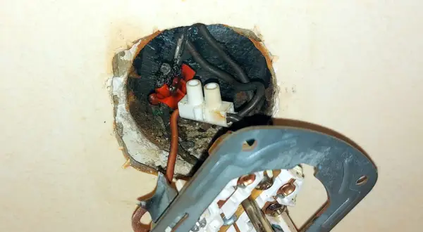 Widoczne iskrzenie w gniazdku, spalone przewody i luźne połączenia. Niebezpieczna sytuacja elektryczna.