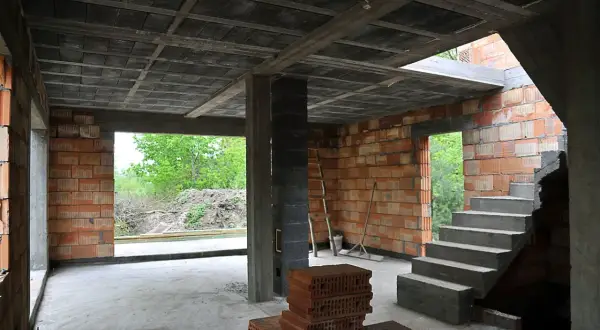 Budowa domu w stanie surowym. Widać betonowy strop typu ackerman, ściany z pustaków ceramicznych, schody i materiały budowlane.
