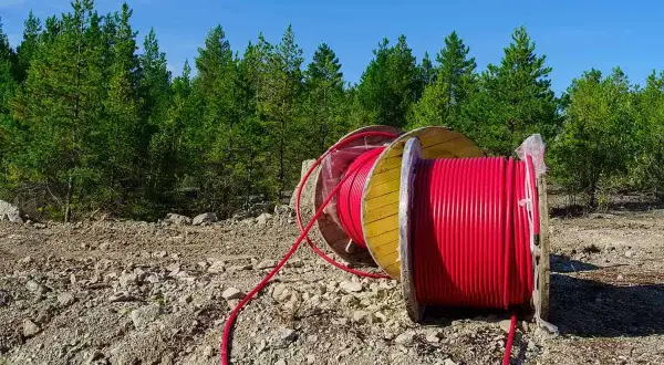 Uzbrojenie działki krok po kroku: duża szpula z czerwonym kablem leży na kamienistym terenie, w tle las i błękitne niebo.
