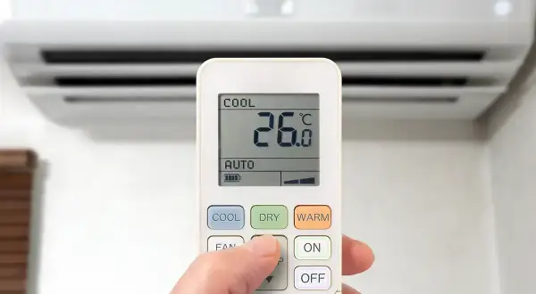 Dłoń steruje pilotem klimatyzacji, wybierając funkcje chłodzenia (COOL), osuszania (DRY) lub grzania (WARM), by dostosować temperaturę.