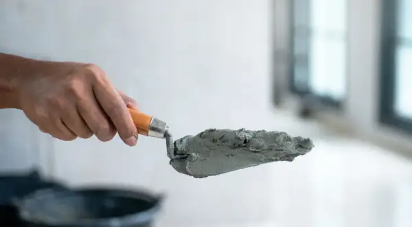 Dłoń trzyma kielnię z masą betonową, przygotowując się do pracy. Dowiedz się, jak zrobić suchy beton.