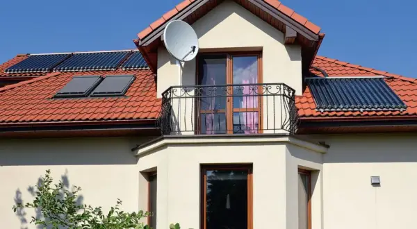 Elegancki wykusz w domu z balkonem i oknami, na dachu panele słoneczne i antenę satelitarną.