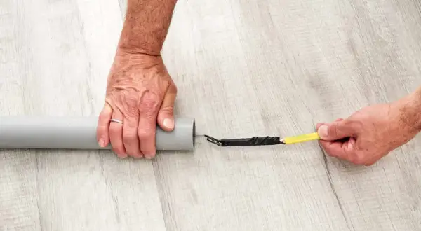 Ręce przygotowują kabel do przeciągnięcia przez peszel. Końcówka kabla owinięta taśmą jest wkładana do szarej rury.