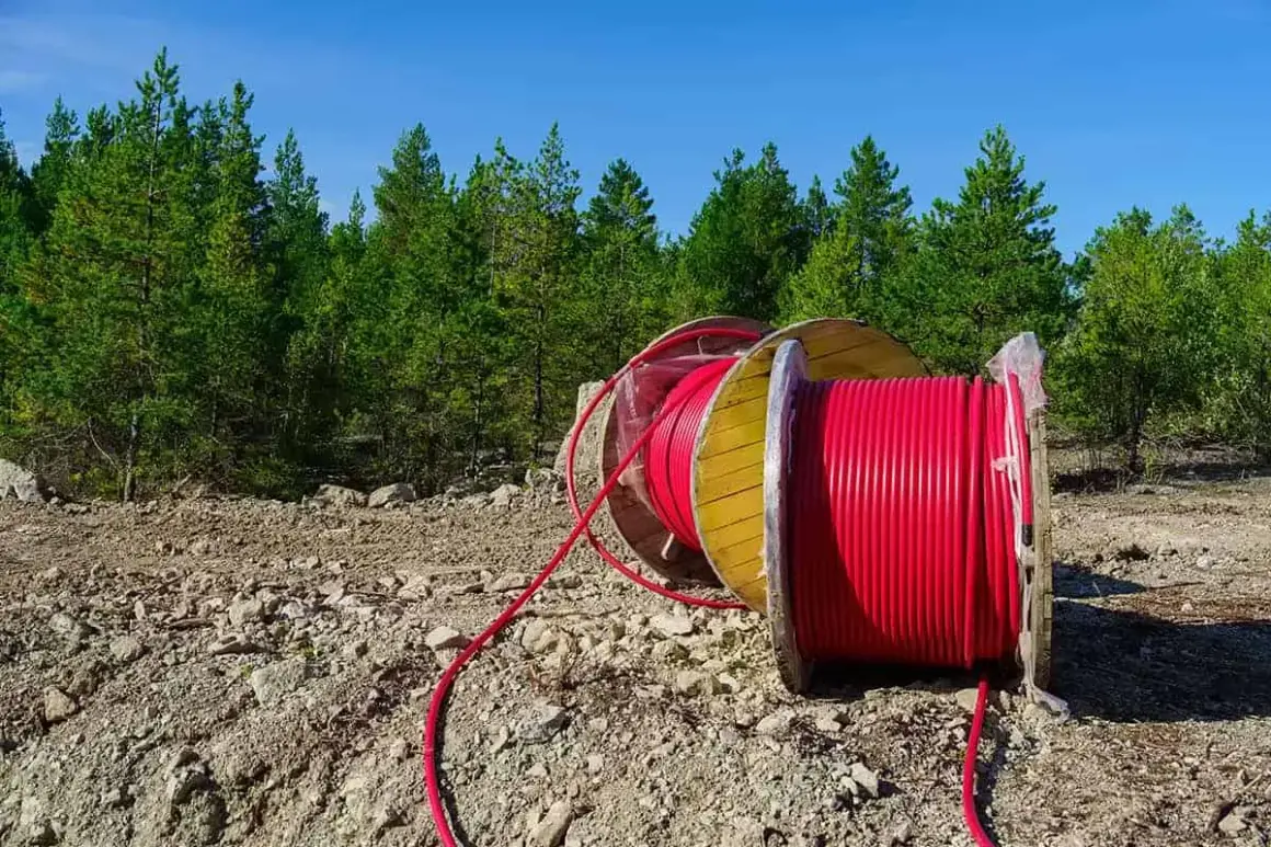 Uzbrojenie działki krok po kroku: duża szpula z czerwonym kablem leży na kamienistym terenie, w tle las i błękitne niebo.