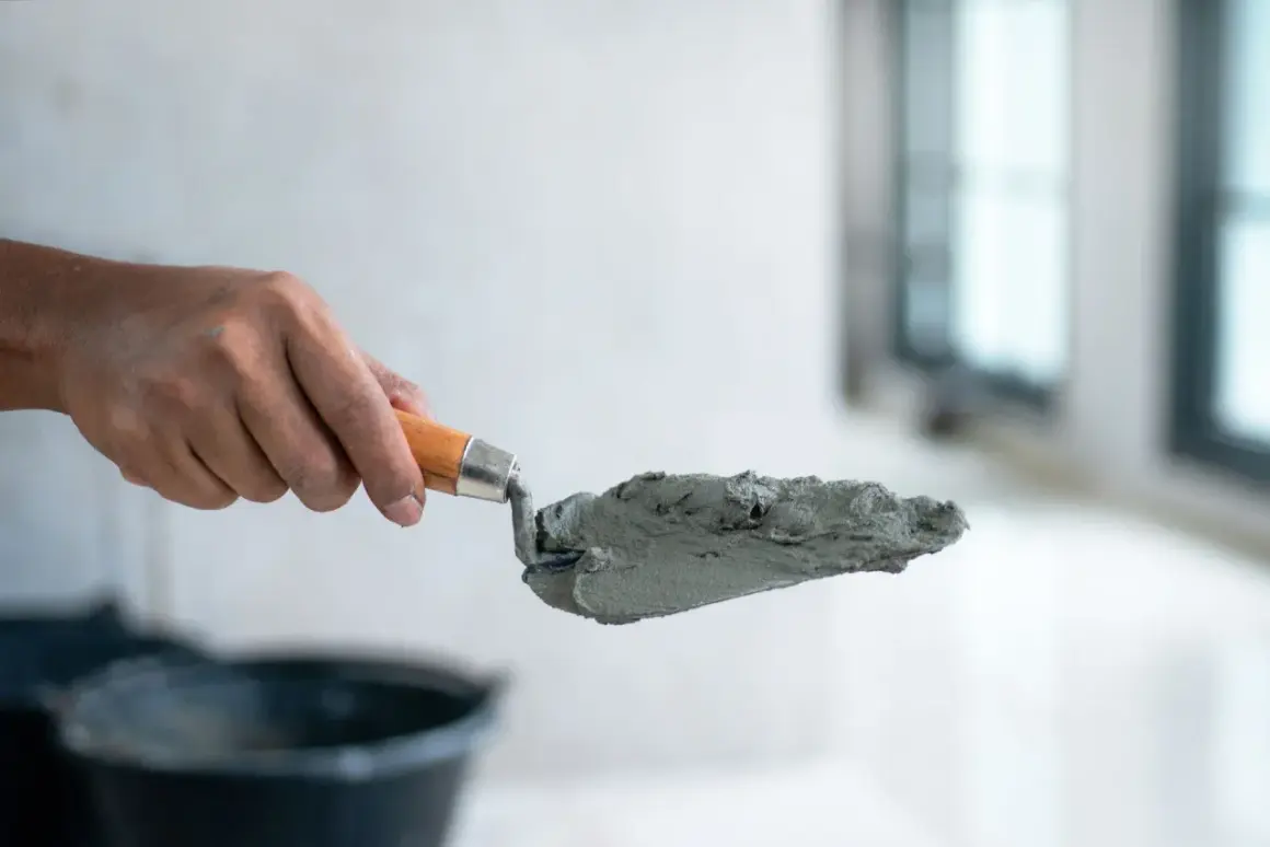 Dłoń trzyma kielnię z masą betonową, przygotowując się do pracy. Dowiedz się, jak zrobić suchy beton.