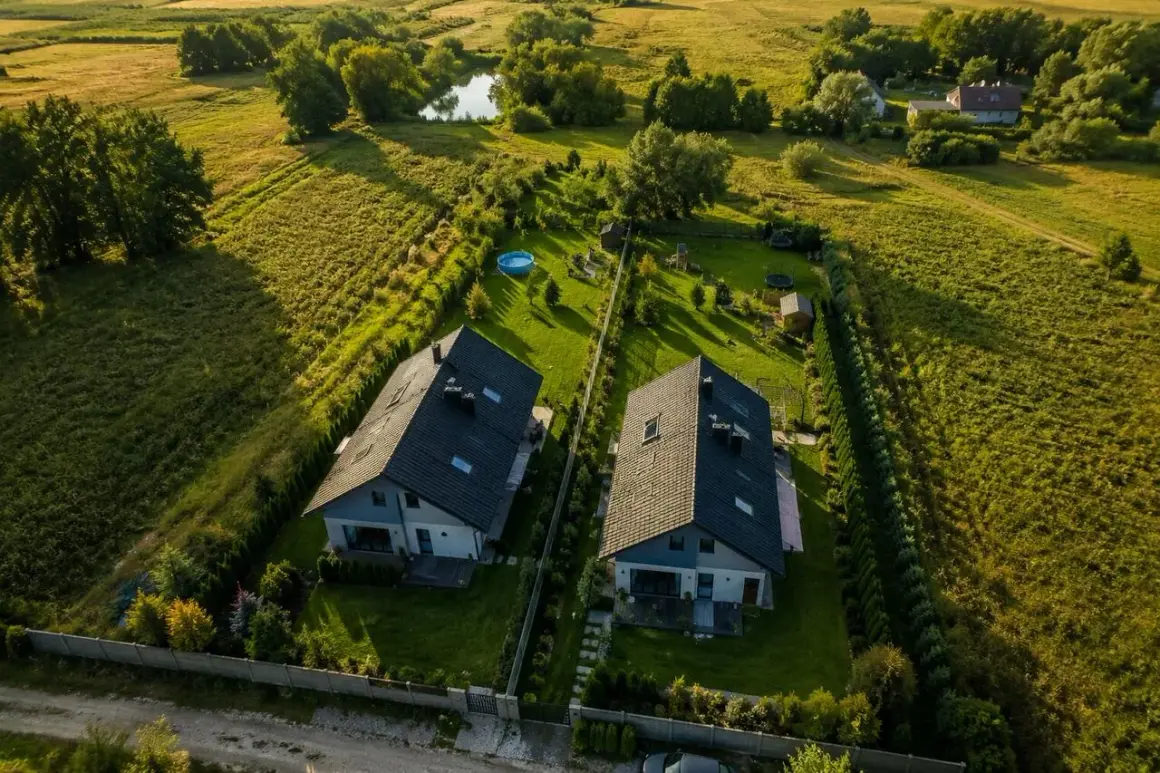 Dwa nowoczesne domy na tle zielonych pól i stawu. Widać plac zabaw i basen. Idealne miejsce na scalenie działek i stworzenie wymarzonej przestrzeni.