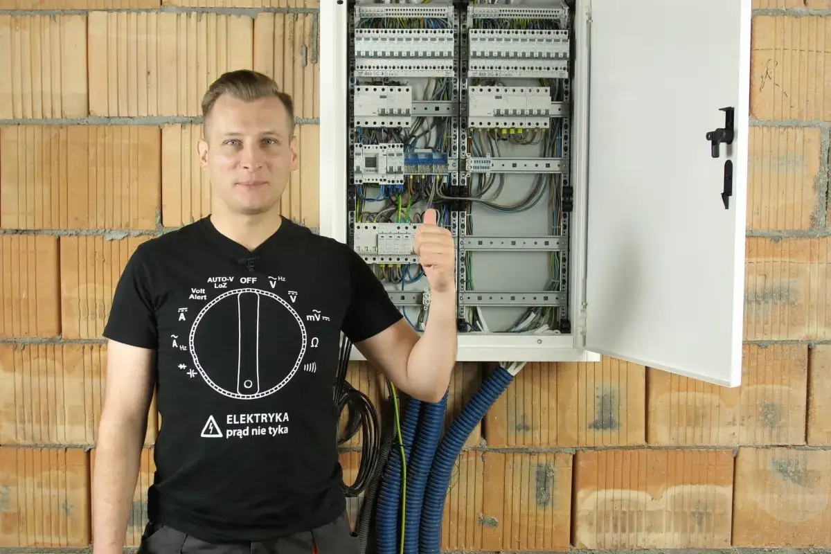 Elektryk pokazuje rozdzielnicę elektryczną, wyjaśniając, co to jest RCBO. Kciuk w górę.