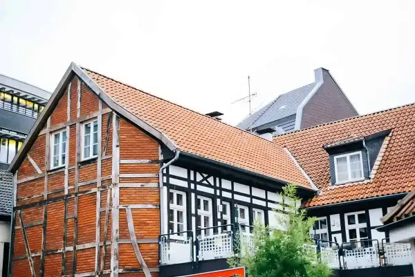 Urokliwy dom szachulcowy z ceglanymi ścianami i białymi belkami, otoczony innymi budynkami i zielenią.