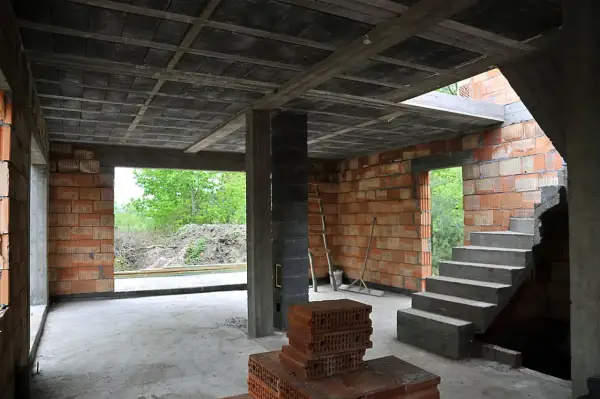 Budowa domu w stanie surowym. Widać betonowy strop typu ackerman, ściany z pustaków ceramicznych, schody i materiały budowlane.