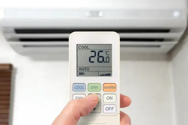 Dłoń steruje pilotem klimatyzacji, wybierając funkcje chłodzenia (COOL), osuszania (DRY) lub grzania (WARM), by dostosować temperaturę.