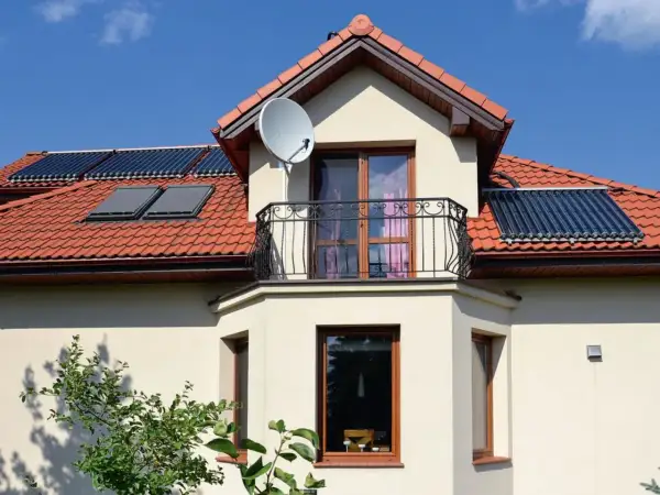 Elegancki wykusz w domu z balkonem i oknami, na dachu panele słoneczne i antenę satelitarną.